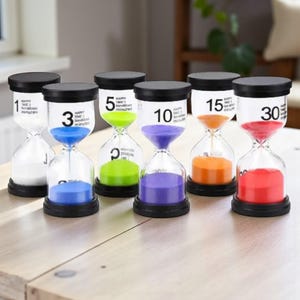 Könnte beinhalten: Sechs Sanduhren mit schwarzen Deckeln und Sockeln. Jede Uhr enthält farbigen Sand: weiß, blau, grün, lila, orange und rot. Die Uhren sind mit der Zeit in Minuten beschriftet: 1, 3, 5, 10, 15 und 30.