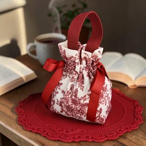 Puede incluir: Una taza de cerámica blanca con un asa negra y el texto "But First, Coffee" en un estilo manuscrito. La taza está sobre una superficie blanca. La taza mide 10 cm de alto.