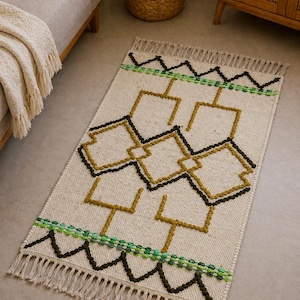 May include: Cream-coloured rectangular rug with a geometric pattern in black, olive green, and gold. The rug has a fringed edge and a repeating design of connected shapes. A decorative accent for any room.