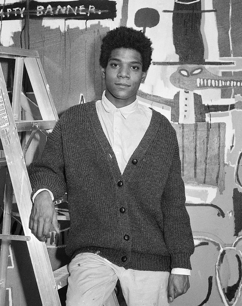 Puede incluir: Una fotograf&iacute;a en blanco y negro de un joven que lleva un c&aacute;rdigan gris y una camisa blanca. Est&aacute; de pie frente a una pared con pinturas abstractas. El texto "EMPTY BANNER" es visible en la pared.