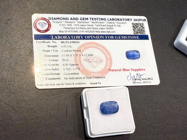 Puede incluir: Un zafiro azul con talla mixta coj&iacute;n, con un peso de 4,05 quilates. La gema se muestra en una caja blanca junto a un certificado de laboratorio. El certificado proporciona detalles, incluidas las dimensiones de 11,90 x 7,76 x 4,12 mm.