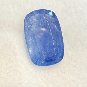 Puede incluir: Una gema azul de forma rectangular con bordes redondeados. La gema es transl&uacute;cida, con estructuras internas visibles y una superficie pulida. El color es un azul profundo y saturado, con sutiles variaciones tonales.