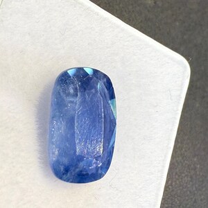 Puede incluir: Una gema azul facetada, de forma ovalada. La gema es de un azul profundo y saturado con un ligero brillo, sobre un fondo blanco. El corte de la piedra crea m&uacute;ltiples facetas que reflejan la luz.