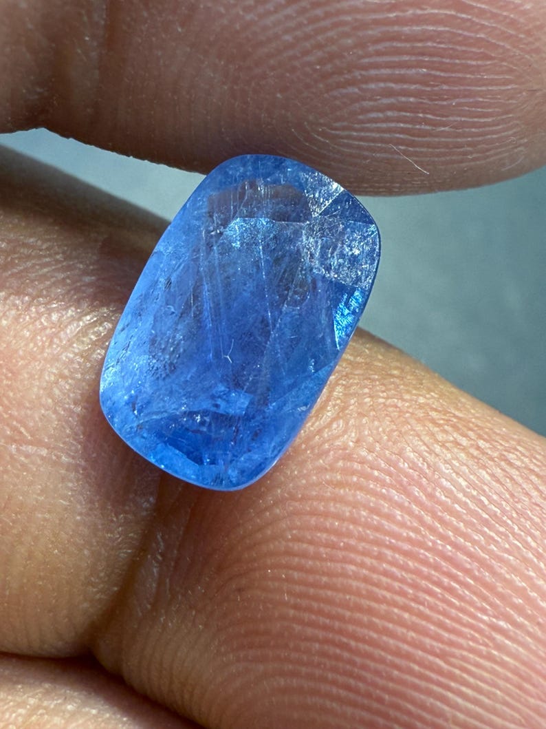 Puede incluir: Una gema azul brillante, de forma rectangular con bordes redondeados. La superficie est&aacute; facetada, captando la luz y revelando patrones internos. El color es un azul profundo y saturado.