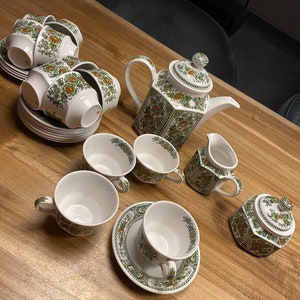 May include: A complete tea set with white cups, saucers, a teapot, creamer, and sugar bowl. The set features a floral design in orange and green. The tea set is arranged on a wooden table, showcasing a classic tea party aesthetic.