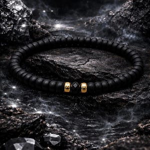 Peut inclure: Un bracelet composé de perles sphériques noires mates disposées en boucle continue. Le design comprend deux entretoises cylindriques dorées polies entourant une perle noire unique à facettes au centre du cordon de perles.