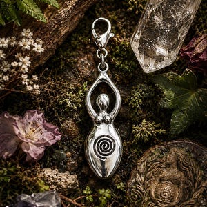 May include: A silver pendant in the shape of a stylized female figure with arms raised, featuring a spiral design on the torso. The pendant is set against a backdrop of moss, crystals, and flowers, creating an earthy aesthetic.
