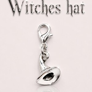 May include: A silver-colored charm in the shape of a witch's hat, with a lobster clasp. The word "Witches hat" is above the charm. The charm is on a light pink background.