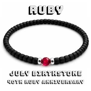 May include: Black beaded bracelet with a faceted ruby gemstone center. The word "RUBY" is at the top, and "JULY BIRTHSTONE 40TH RUBY ANNIVERSARY" is at the bottom. The bracelet is a jewelry item.