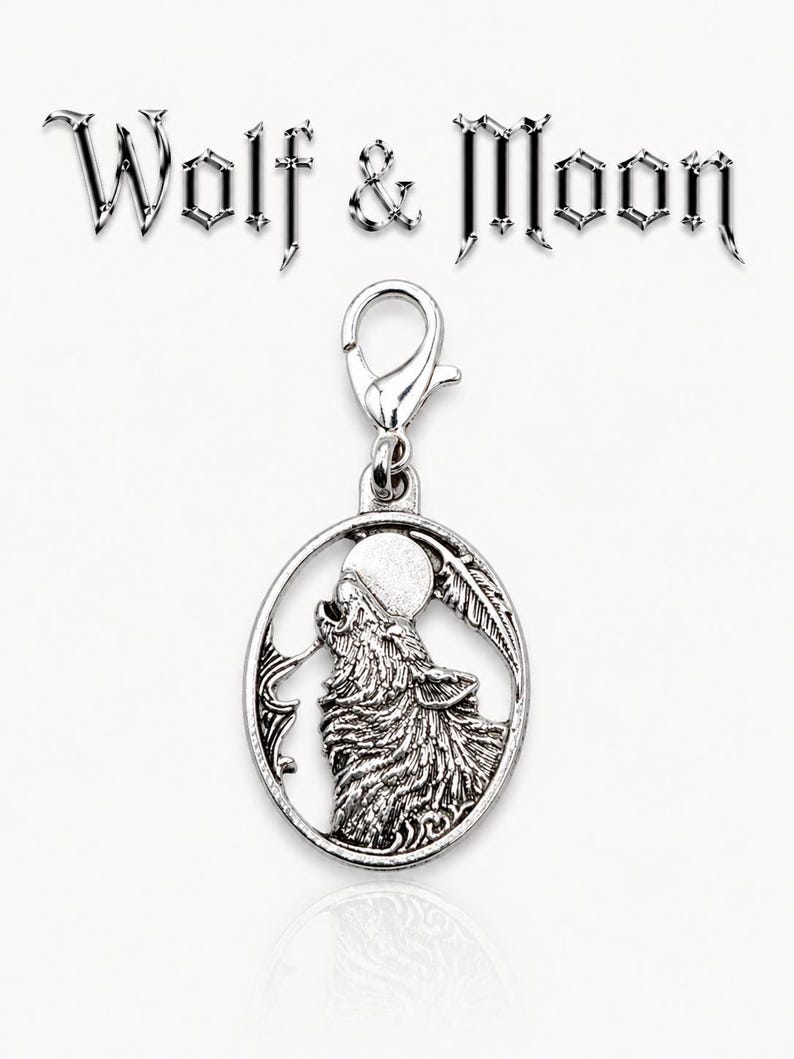 May include: Silver-toned charm with a howling wolf silhouette, a full moon, and a feather design within an oval frame. The charm is attached to a clasp. The words "Wolf & Moon" are above the charm.