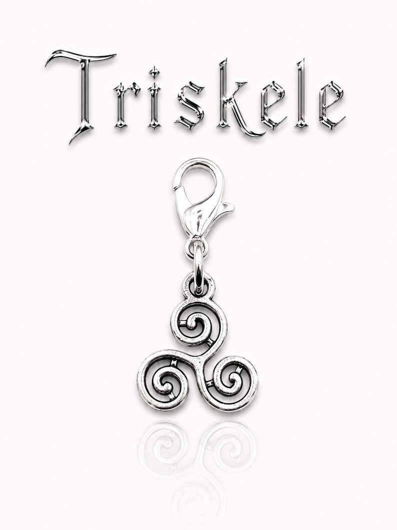 May include: A silver-colored Triskele charm with a lobster clasp. The charm features a three-spiral design, and the word "Triskele" is displayed above the charm in a metallic font. The charm is displayed on a white background.