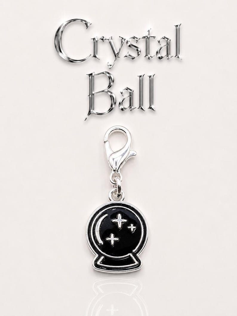 May include: A silver-colored charm with a black crystal ball design, featuring three white stars inside. The charm is attached to a silver clasp. The words "Crystal Ball" are displayed above the charm in a metallic font.