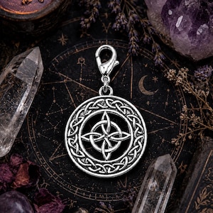 May include: A silver-toned metal charm featuring a circular frame with an intricate Celtic knot pattern surrounding a central four-pointed knot design. The charm includes a small lobster claw clasp attached to the top for easy attachment.
