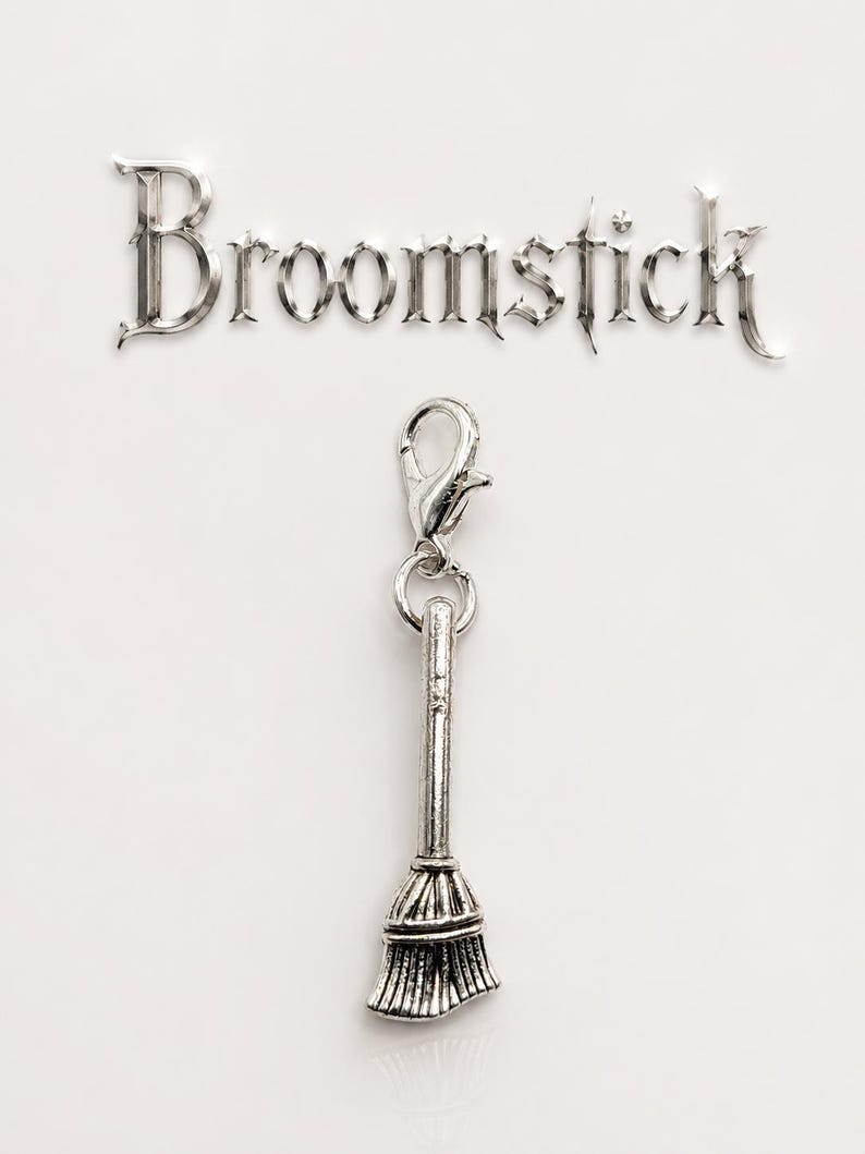 May include: A silver-colored charm in the shape of a broomstick, attached to a clasp. The word "Broomstick" is displayed above the charm in a decorative font. The background is plain white.