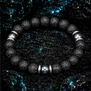 Peut inclure: Un bracelet composé de perles rondes en pierre de lave noire poreuse, alternées avec des entretoises métalliques argentées lisses et trois perles sphériques gris foncé polies réparties sur le cordon élastique circulaire.