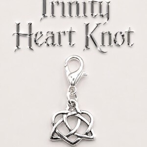 May include: A silver-colored charm with a Trinity Heart Knot design, suspended from a lobster clasp. The words "Trinity Heart Knot" are displayed in a metallic font above the charm on a white background.