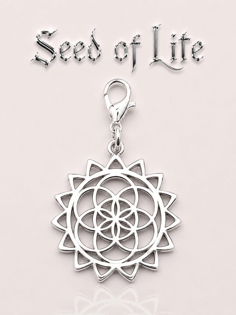 May include: A silver charm pendant with a sunburst design and a central geometric pattern. The pendant is attached to a clasp. The words "Seed of Life" are displayed above the charm in a stylized font.