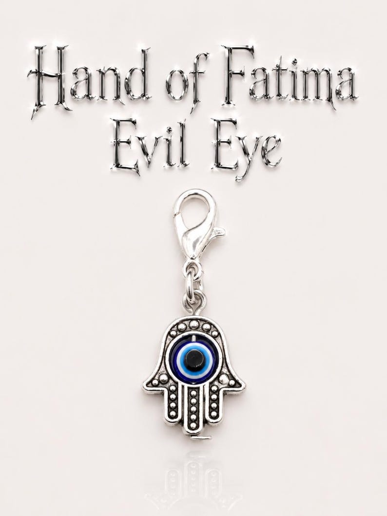 May include: A silver-toned charm with a Hand of Fatima design and an evil eye symbol. The charm has a lobster clasp and features a blue and black eye in the center of the hand. The words "Hand of Fatima Evil Eye" are above the charm.