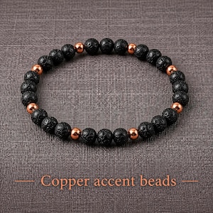 May include: A circular bracelet composed of alternating black porous lava beads and smooth, polished copper-coloured metallic accent beads. The beads are arranged in a repeating pattern, creating a textured and metallic contrast throughout the piece.