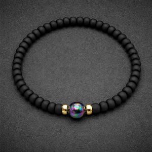 May include: A beaded bracelet featuring a continuous loop of matte black spherical beads. The design is centred with a single iridescent, multi-coloured bead flanked by two small, polished gold-tone metallic spacer beads.