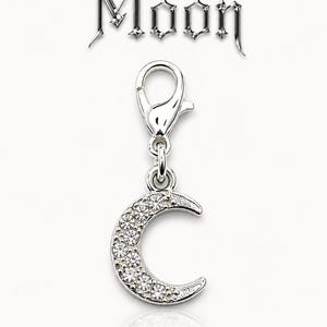 May include: A silver-colored charm in the shape of a crescent moon, encrusted with clear crystals. The charm is attached to a clasp. The word "Moon" is displayed above the charm in a decorative font.