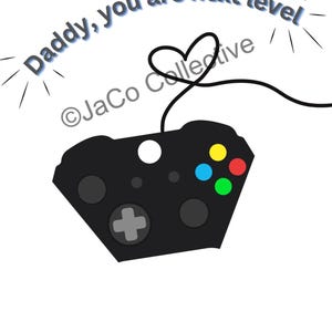 May include: A black video game controller with colorful buttons and a heart-shaped cable. The text "Daddy, you are next level" is arched above the controller. The image has a white background.