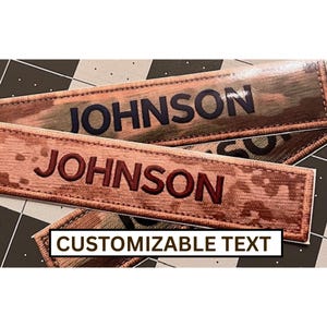 May include: Two rectangular patches with the name "JOHNSON" in dark blue and maroon lettering. The patches have a camouflage pattern in shades of brown, green, and tan. The text "CUSTOMIZABLE TEXT" is displayed in a white box.