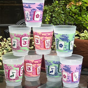 May include: A stack of clear plastic cups with colorful designs. Each cup features a different design, including a floral motif, a crane, and the word "Joker". The cups have a pink, orange, and green color scheme.