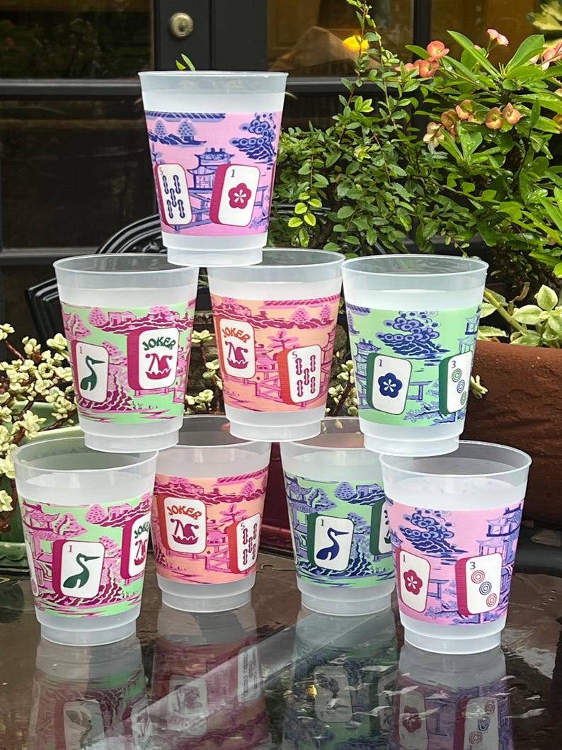 May include: A stack of clear plastic cups with colorful designs. Each cup features a different design, including a floral motif, a crane, and the word "Joker". The cups have a pink, orange, and green color scheme.