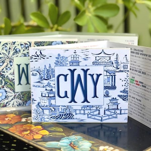 May include: A folded card featuring a blue and white chinoiserie pattern with a central monogram reading CWY. The interior panel displays a printed list of game values and scoring combinations for Mah Jongg, including text like Dragons and Pairs.