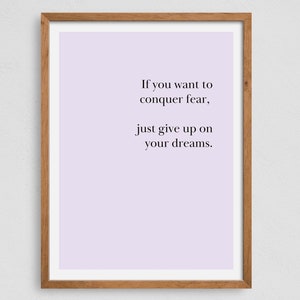 May include: A motivational quote printed on a light purple background in a wooden frame. The quote reads: "If you want to conquer fear, just give up on your dreams."