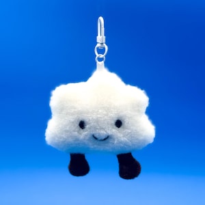 May include: A white cloud-shaped plush keychain with a smiling face and small black feet. The keychain has a silver metal clasp for easy attachment. The plush toy is set against a bright blue background.