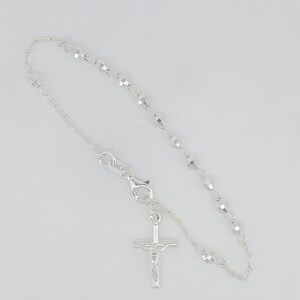 May include: A silver rosary bracelet with a crucifix charm. The bracelet features small, faceted beads and a delicate chain.