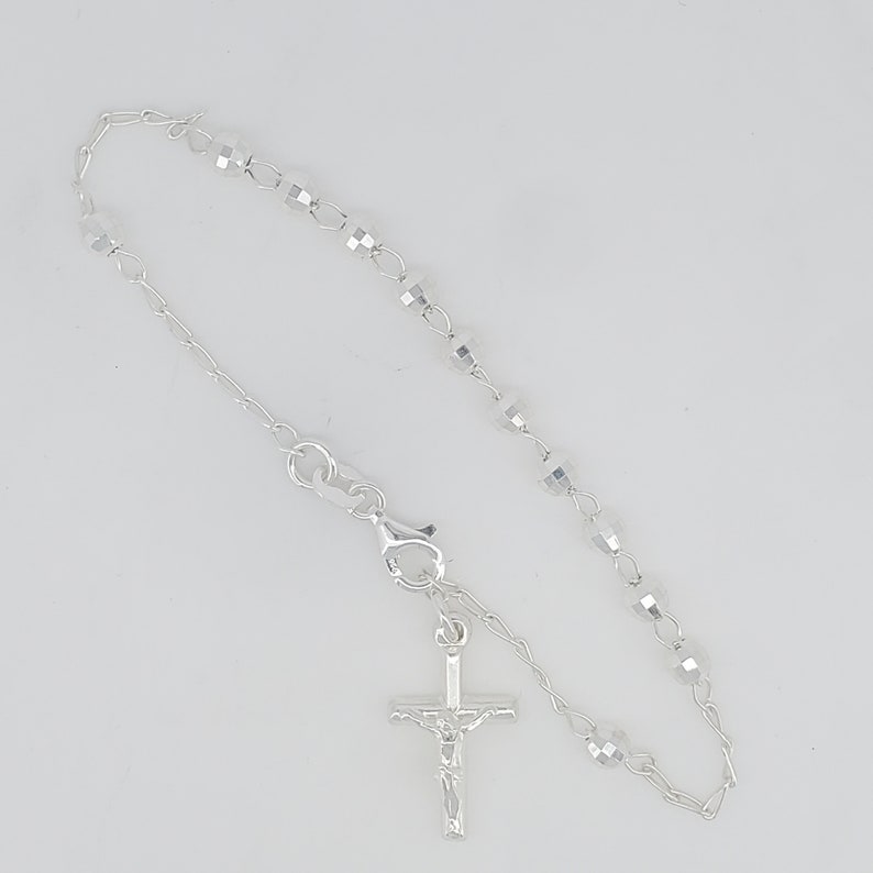 May include: A silver rosary bracelet with a crucifix charm. The bracelet features small, faceted beads and a delicate chain.