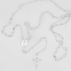 Pode incluir: Um colar de ros&aacute;rio de prata com um crucifixo de prata e um pingente oval de prata com uma imagem religiosa.