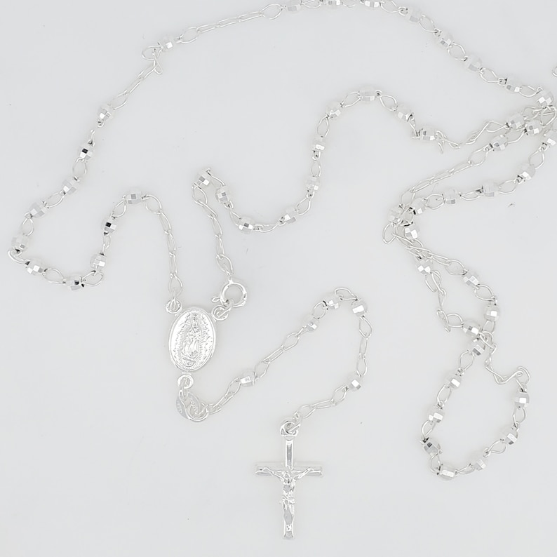 Pode incluir: Um colar de ros&aacute;rio de prata com um crucifixo de prata e um pingente oval de prata com uma imagem religiosa.