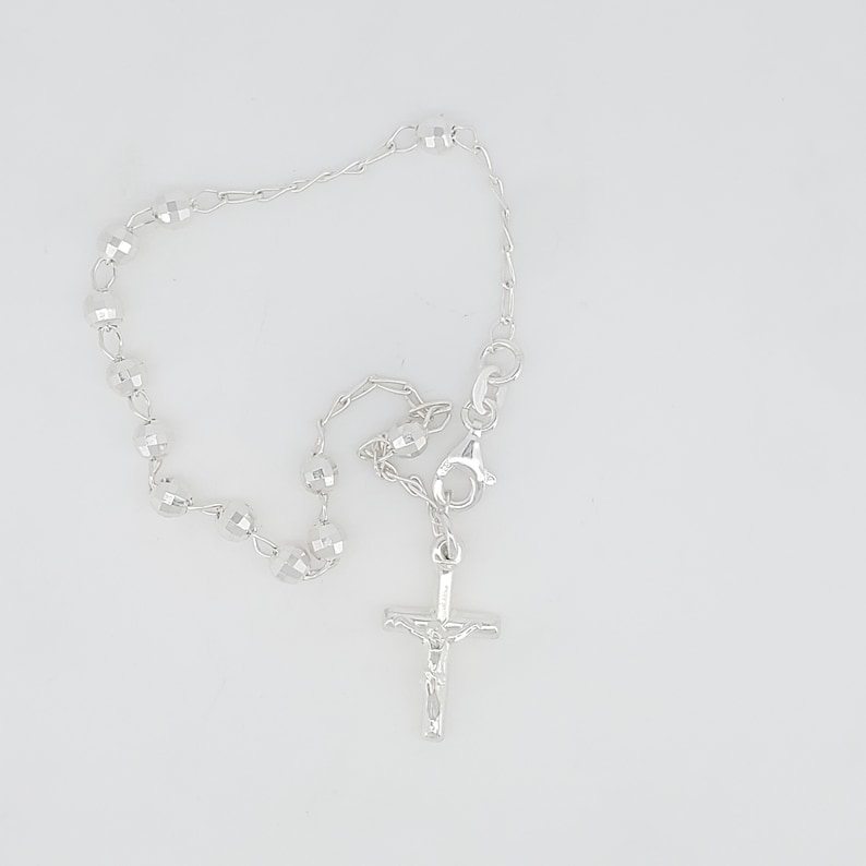 May include: A silver rosary bracelet with a small silver crucifix charm. The beads are faceted and the chain is delicate.