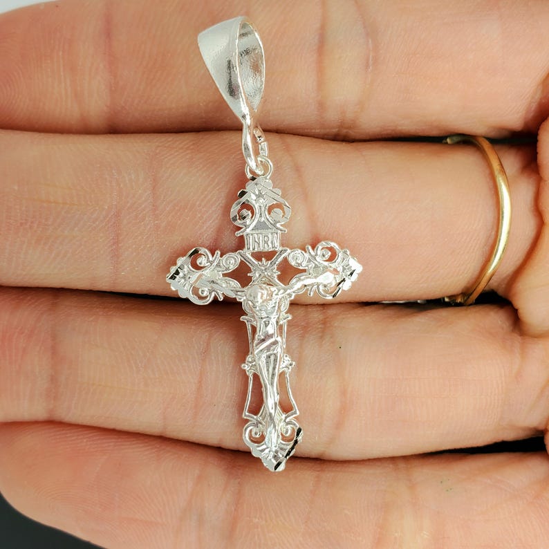 May include: Silver filigree crucifix pendant with a detailed depiction of Jesus Christ on the cross. The pendant features a bail for attaching to a chain.