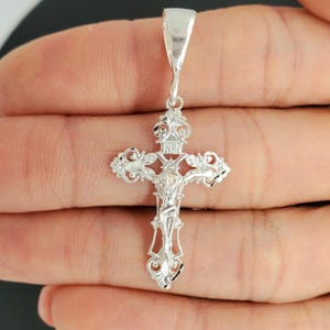 May include: Silver filigree cross pendant featuring a detailed depiction of Jesus Christ on the cross. The cross has intricate floral designs and the inscription "INRI" at the top.