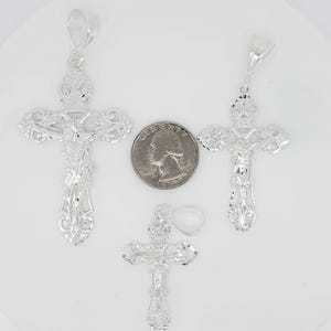 May include: Three silver filigree cross pendants of varying sizes. The largest cross is slightly larger than a UK 20 pence coin.