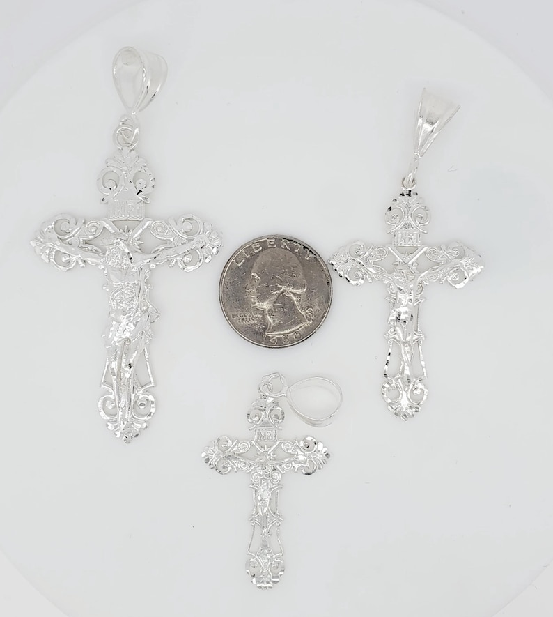 May include: Three silver filigree cross pendants of varying sizes. The largest cross is slightly larger than a UK 20 pence coin.