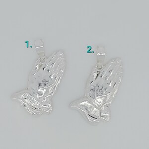 May include: Two silver praying hands charms with a loop for attaching to a necklace or bracelet.