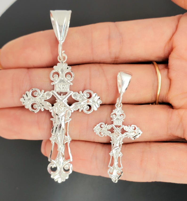 May include: Two silver filigree cross pendants with a crucifix design. The larger cross is approximately 5 cm tall and the smaller cross is approximately 2.5 cm tall.