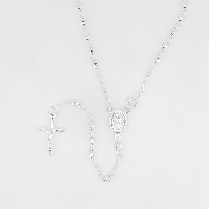 Pode incluir: Um colar de ros&aacute;rio de prata com um crucifixo de prata e um pingente de prata com a Virgem Maria.