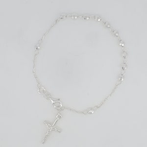 May include: A silver bracelet with a small silver cross charm and clear crystal beads.