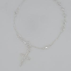 May include: A silver bracelet with a small silver cross charm and clear crystal beads.