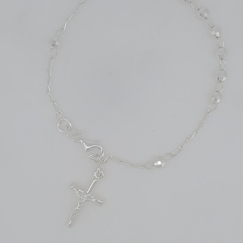May include: A silver bracelet with a small silver cross charm and clear crystal beads.