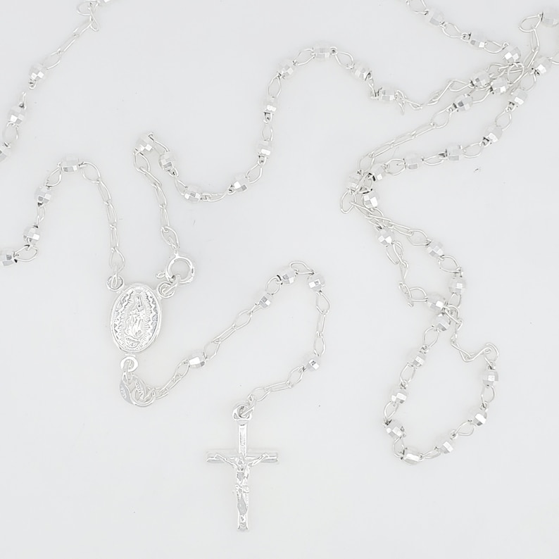 Pode incluir: Um colar de ros&aacute;rio de prata com um crucifixo de prata e um pingente de prata com uma imagem religiosa. As contas do ros&aacute;rio s&atilde;o facetadas e t&ecirc;m um acabamento brilhante.