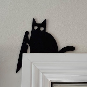 May include: Black silhouette of a cat holding a knife, mounted on a white door frame.