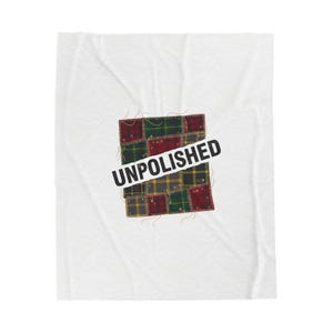 Pode incluir: Um cobertor branco com um retalho quadrado de tecido xadrez vermelho, verde e amarelo. O texto "UNPOLISHED" está impresso em preto sobre o retalho xadrez.